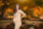 Pregnant woman in a flowing dress cradling her baby bump, captured in soft, natural light outdoors.