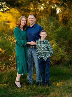 mom, dad and son posing for a family picture at Murrell Park wearing green and blue tones.