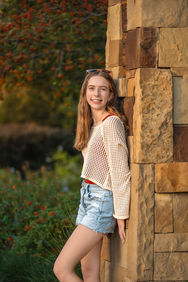 DFW senior photography session with a senior leaning against a stone wall in a garden setting