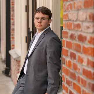 Senior boy in gray suit posing by brick wall in Downtown McKinney urban senior session
