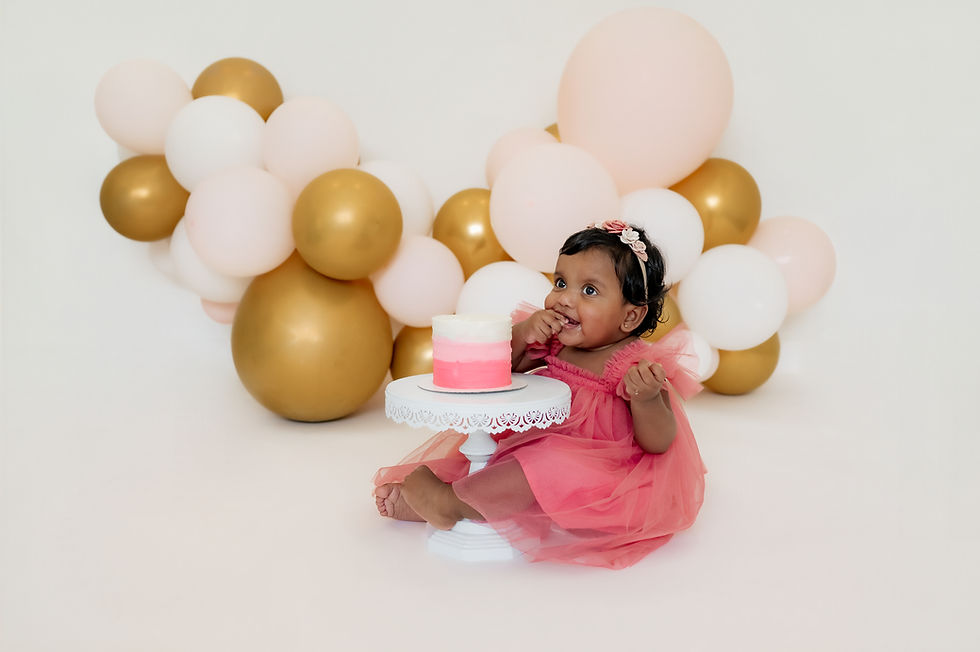 Milestone session in DFW studio, one-year-old girl in pink dress with ombré pink cake and festive balloon garland.