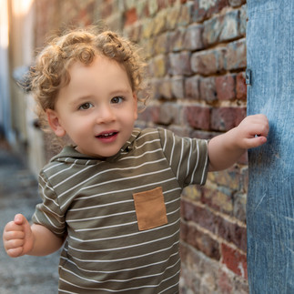 two year old boy posing for milestone session in downtown McKinney wearing striped top and khaki shorts