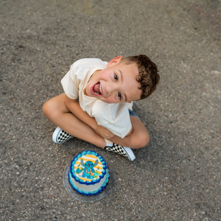 Five-year-old boy sitting cross-legged on the ground with a playful pose next to his Lilo & Stitch birthday cake in McKinney.