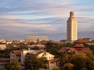 UT Austin campus skyline with a tall tower under a cloudy sky. Buildings feature red roofs and trees surround the area, creating a peaceful ambiance.