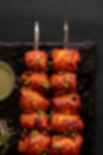 Close-up of chargrilled chicken skewers on matte black slate with moody lighting — highlighting premium restaurant photography using deep tones and rich contrast.