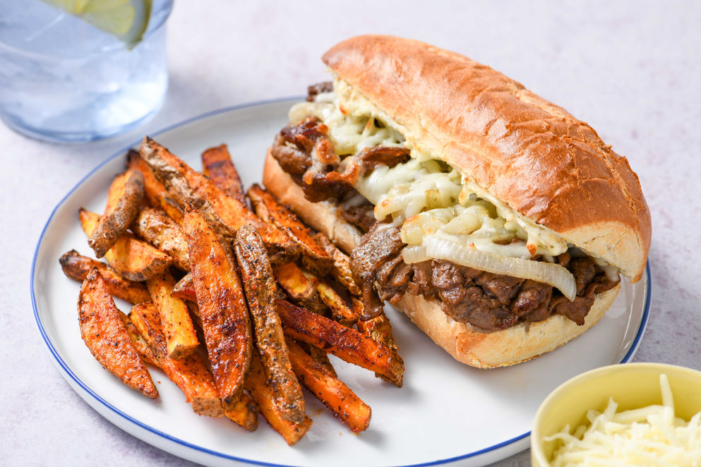 Three-quarter angle Philly cheesesteak sandwich with fries on white plate commercial food photography Chicago