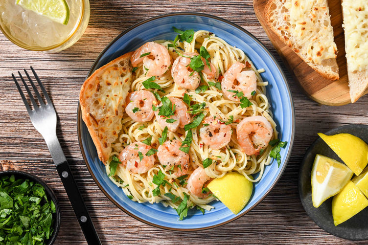 Three-quarter angle shrimp pasta dish with lemon and herbs in blue bowl rustic table commercial food photography