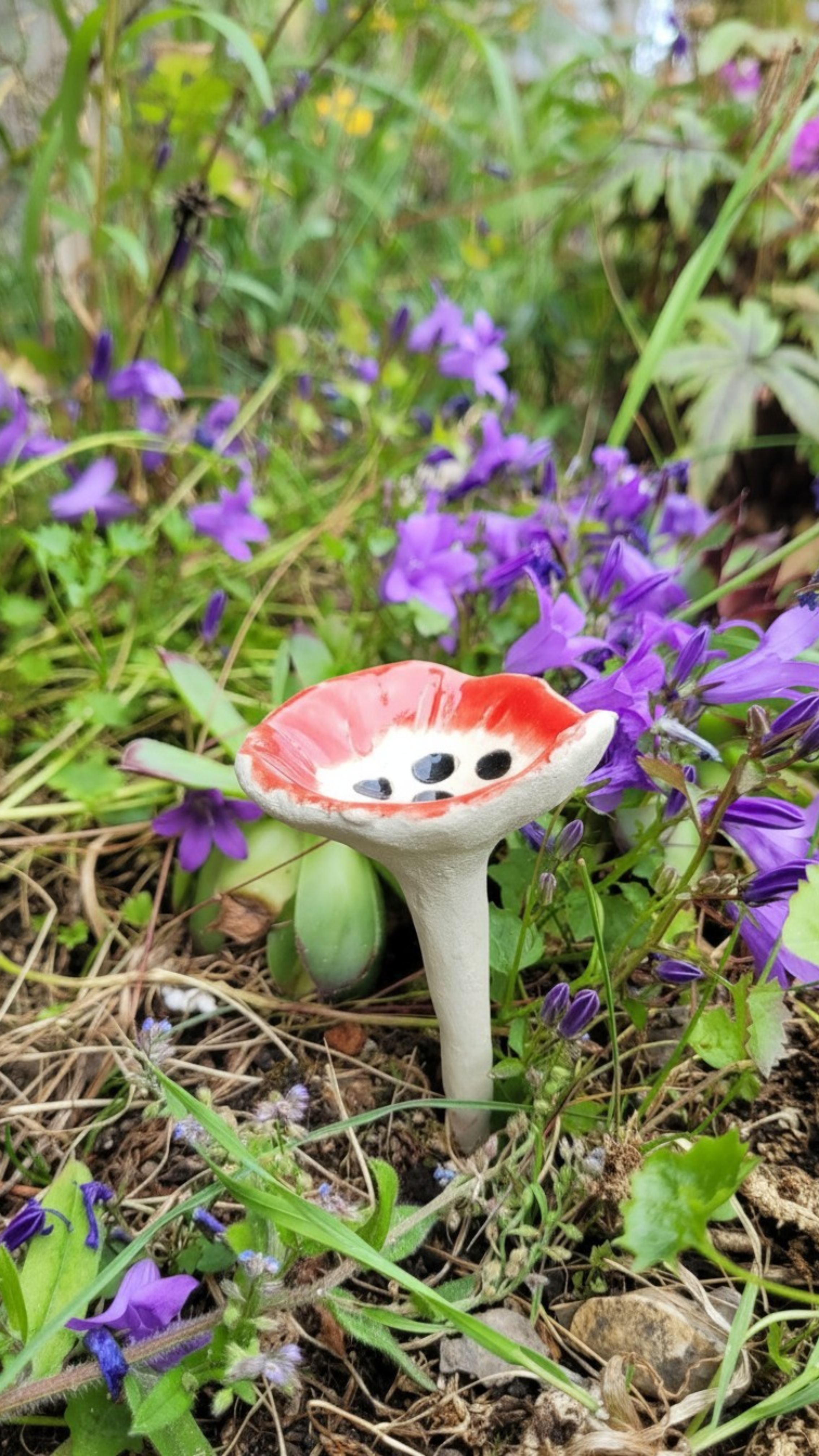 Abreuvoir à insectes en céramique rouge planté dans un jardin fleuri