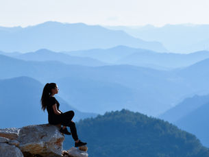 Woman sitting quietly on a mountain ledge — image for “Your Brain Is Not the Problem. Your Attention Is.”