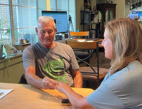 Craig placing a custom emerald cut emerald halo diamond ring on his wife's finger for the first time after seeing the reveal at K. Hollis Jewelers.