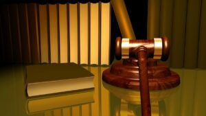 Gavel and book on shiny surface with golden, striped background, suggesting a legal or courtroom setting. Warm lighting creates a serious mood.