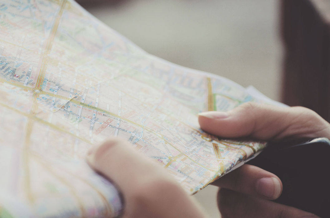 Hands holding a paper road map for GPS tracking.