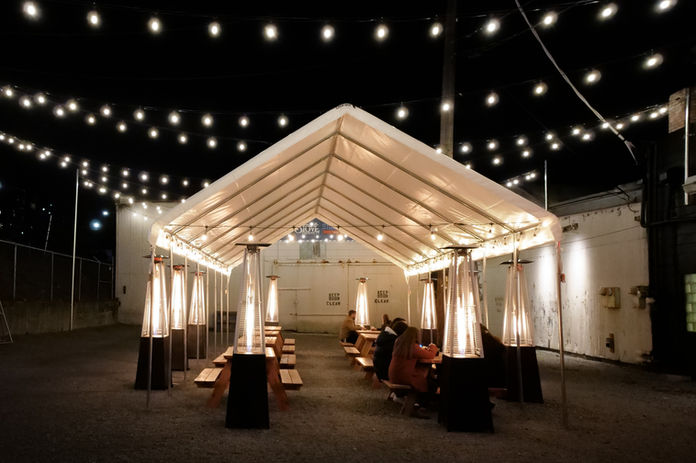 Outdoor patio with tent, heaters, and string lights at night.