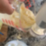 Measuring cup pouring separated mayonnaise into tall container with a hand blender blending mayonnaise back together.
