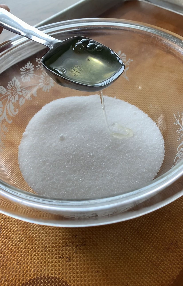 Bowl of sugar and Egg Whites in a spoon about to be dropped into the sugar.
