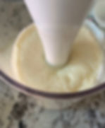 Immersion blender mixing a failed, watery and grainy mayonnaise in a transparent container on a marbled countertop. Smooth texture, kitchen setting.