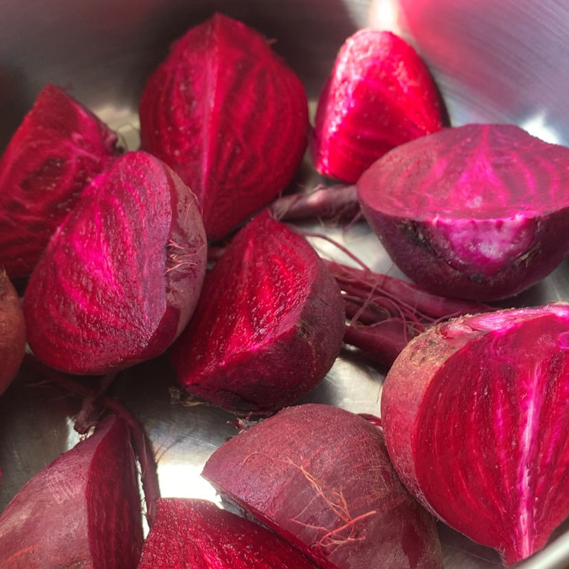 Halved bright red beets in a shiny metal pot, showcasing vibrant color and intricate patterns on their surfaces, fresh and earthy.