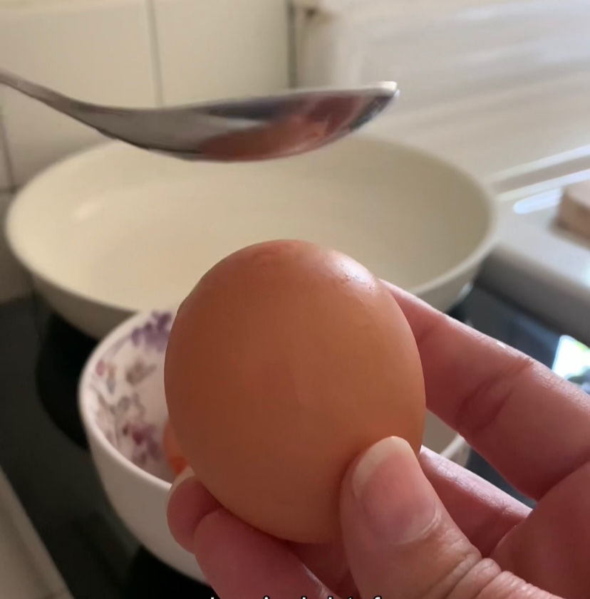 Tapping the bottom rounded side of an uncooked egg to break the membrane