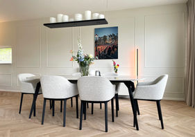 Scandinavisch interieur met lichte kleuren, pastel, eetkamer met tafel en stoelen heel licht en zonnig en plant design hanglamp van kaarsen op een zwart plateau en op een dressoir, beige muren met profielen, Scandinavisch