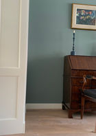 ensuite kast jaren dertig huis met een antiek bureautje en stoel met een prachtig blauwe muur, een vaas met een bloem en kunstwerk en een brandende kaars, mooi interieur