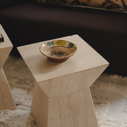 Pale geometric side table topped with a decorative ceramic bowl beside a dark leather sofa.