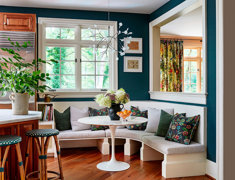 Breakfast nook with deep teal walls, a curved banquette, patterned pillows and a white tulip table.