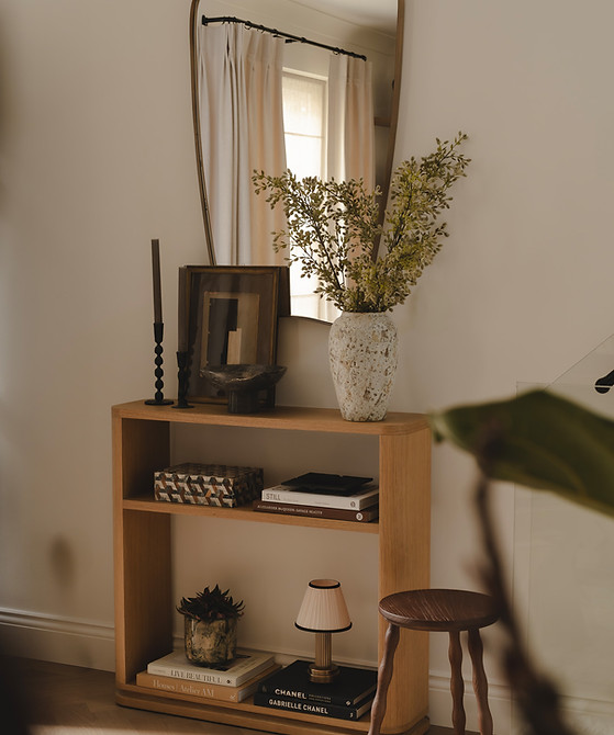 Wood console beneath a tall mirror, styled with leafy branches, framed artwork, candlesticks, and stacked books.