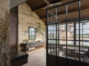Rustic Hill Country bathroom with limestone walls, steel-framed glass enclosure, warm wood ceilings, and natural materials designed by Blair Burton Interiors
