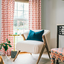 Cozy sitting area with patterned coral drapery, ivory accent chair, and bold blue velvet pillow