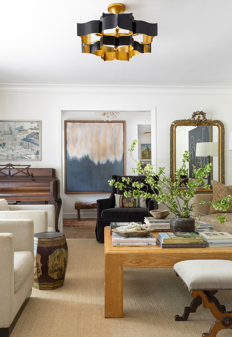 Console table styled with vintage wooden boxes, greenery, and books beneath abstract artwork and ornate gold mirror