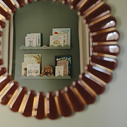 Decorative wood-framed mirror reflecting children’s books on shelves against a green wall.