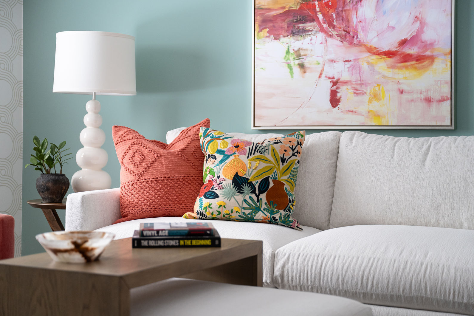 Teal living room with a white couch and colorful pillows with a colorful abstract painting on the wall