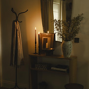 Candlelit wood console styled with framed artwork, leafy branches and stacked books beneath a tall mirror.