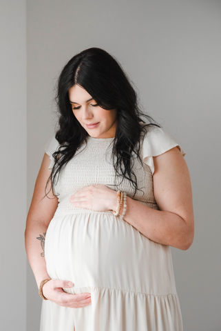 Maternity photo: Woman in white dress, smiling radiantly while holding her pregnant belly