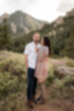 Woman looks up at man lovingly while posing in front of foothills during Boulder, CO sunset engagement session