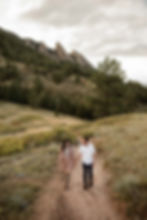 Man and woman hold hands and laugh as they walk the trail during Boulder, CO sunset engagement session