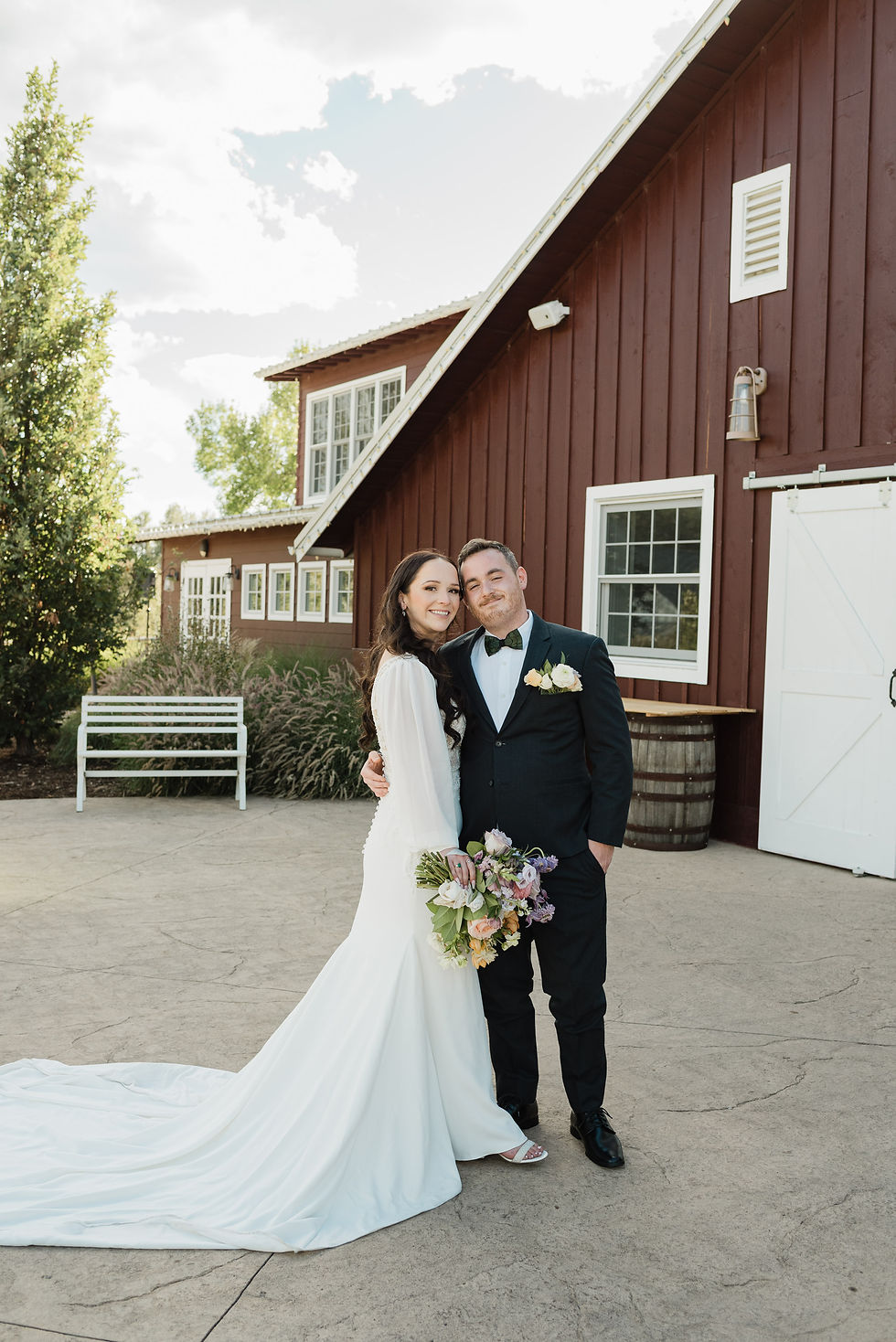 The bride and groom pose in front of the red barn at The Barn at Raccoon Creek in Littleton, CO