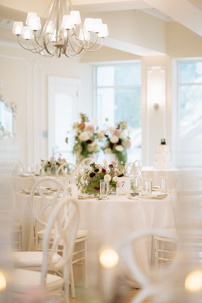 Elegant wedding reception room with white chairs, round tables, floral centerpieces under a chandelier