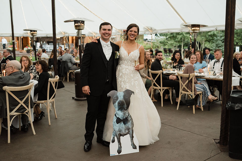 The bride and groom pose with a cardboard cutout of their dog in a bowtie