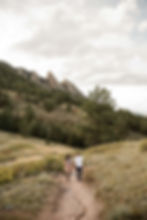 Man and woman hold hands and walk the NCAR trail during Boulder, CO sunset engagement session