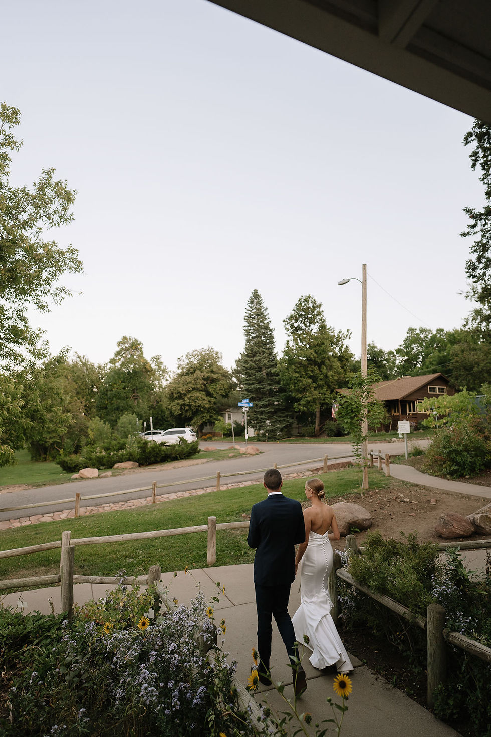 Bride in white gown and groom in dark suit walk away on a garden path at Chautauqua.