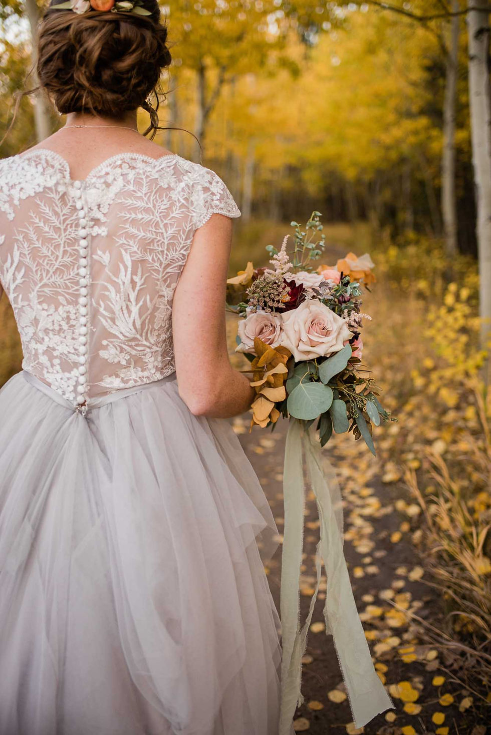 Close up of bride's lace wedding dress and bridal bouquet in the aspen trees