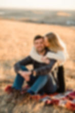 Man smiles at the camera as woman wraps her arms around his neck and kisses his head