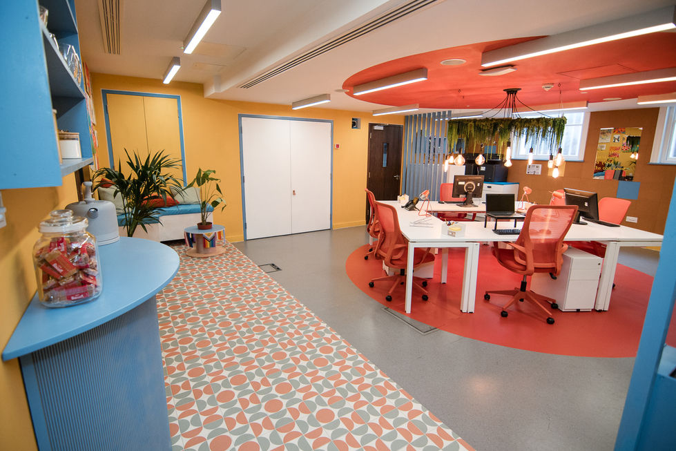 Colourful charity office interior with patterned counter, breakout seating and open-plan workspace designed by Jonni Knight a