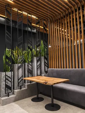 Séparation en lames de bois avec banquette, tables sur mesure et plantes dans un restaurant