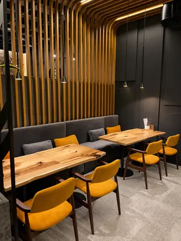 Coin repas de restaurant avec tables en bois naturel, banquette grise et structure en lames de bois