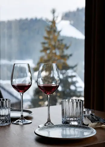 Table de restaurant avec verres de vin devant une baie vitrée donnant sur les montagnes enneigées