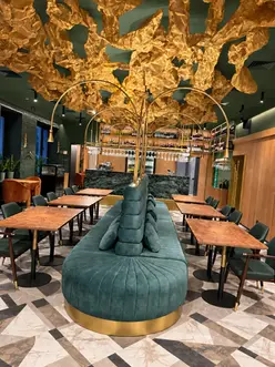 Banquette centrale sculpturale sur mesure dans un restaurant avec tables en bois et plafond doré