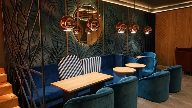 Espace lounge de restaurant avec banquette bleue, fauteuils, tables en bois et luminaires cuivrés