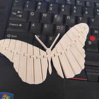 Wooden butterfly, laser cut, rests on a laptop keyboard; design concept, new.